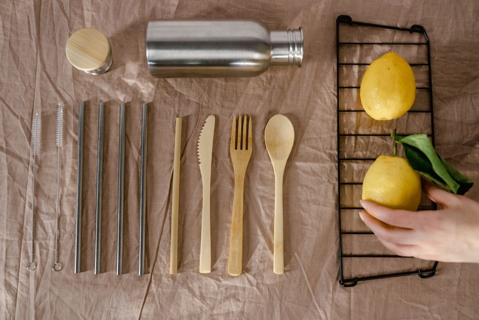 Reusable kitchen utensils, metal straws, a bottle, and lemons arranged on a table.